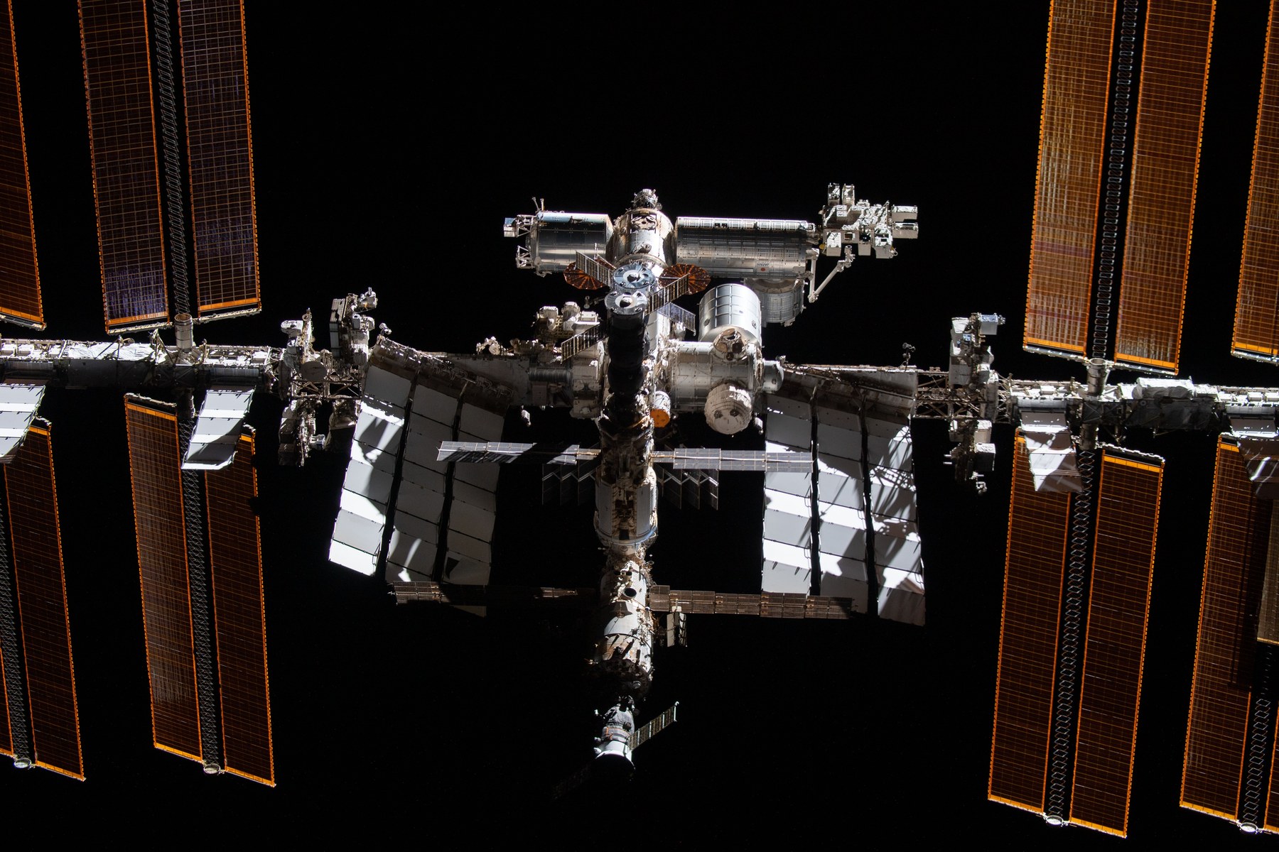 International Space Station modules, white radiators and orange solar arrays against black space during a fly-around