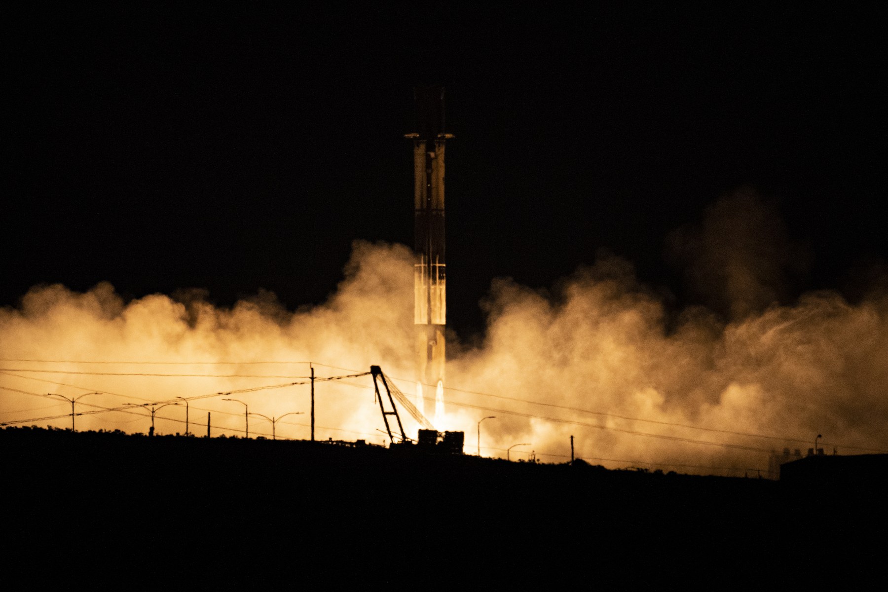 Falcon 9 first-stage booster landing at night at Vandenberg, lit by its engine and surrounded by exhaust clouds
